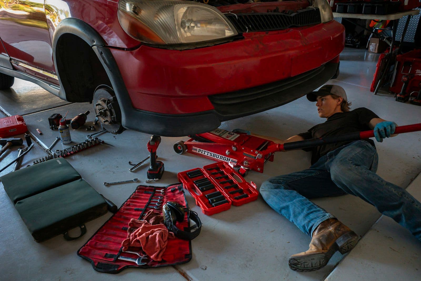 A mechanic working underneath a car on a floor jack, tools spread across the garage floor — Why your auto repair shop needs more than a Facebook page